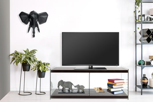 Dieser Fernsehtisch mit Glas Seitenwänden strahlt Eleganz und Transparenz aus. Das gehärtete Glas kontrastiert stilvoll mit den dunkelbraunen, matten Ablageflächen (MDF). Ein TV-Tisch der Serie Elementary, perfekt, um ein einheitliches Gesamtambiente zu schaffen.

